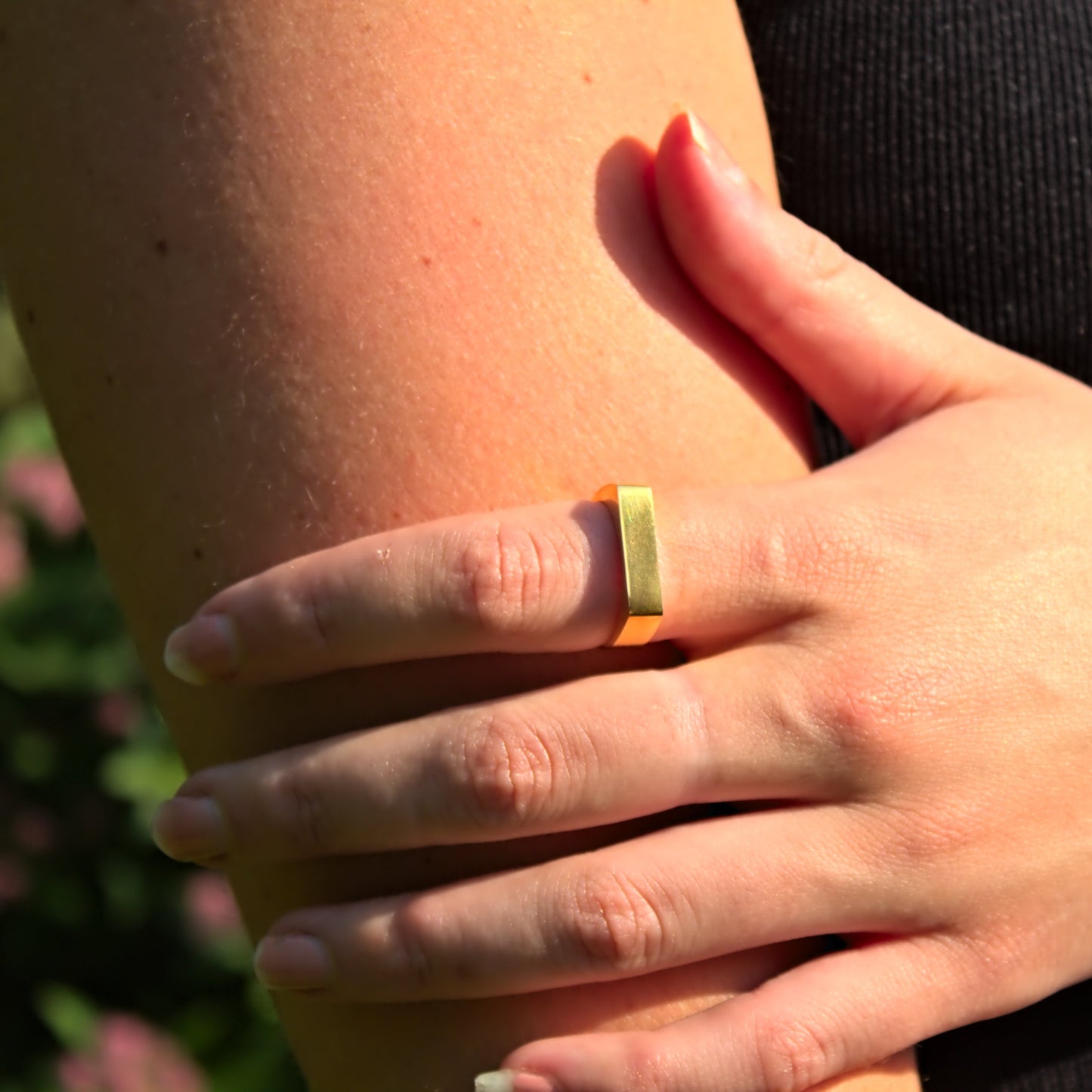 Close up of signet ring on index finger, hand wrapped around other arm. Highlights flat edge of ring.