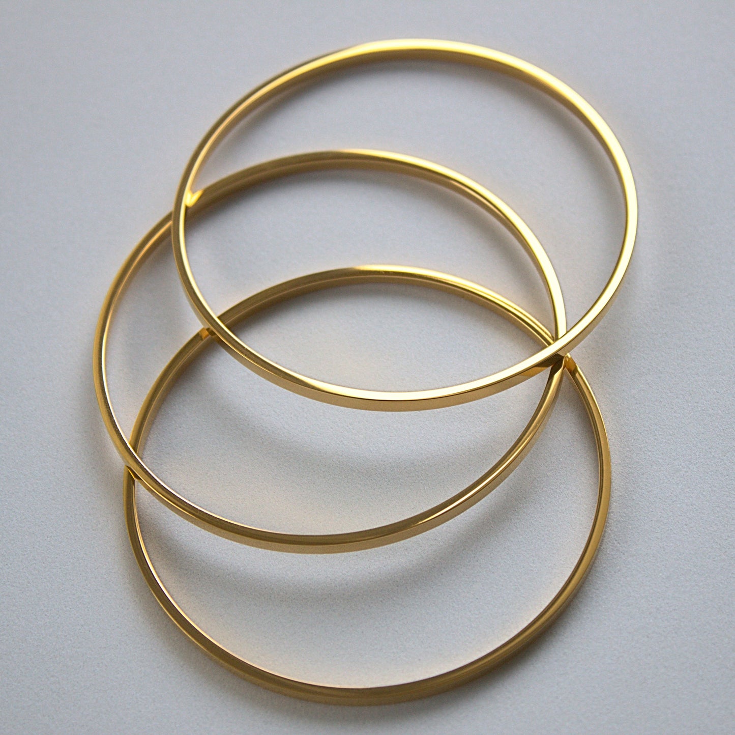 3 flat-edged bangles resting on each other upwards, top profile of all of them, resting on white surface.