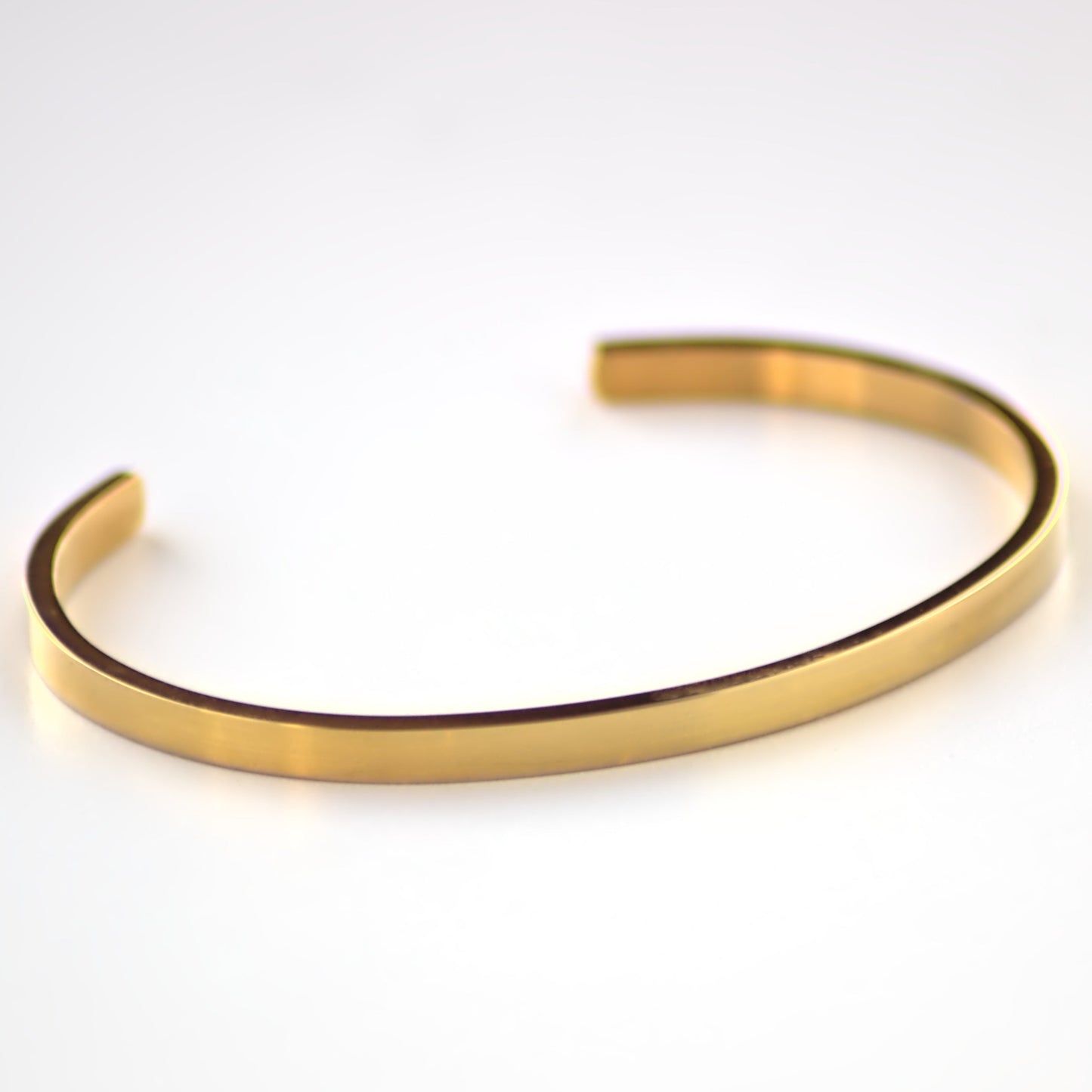 Gold cuff bangle laying flat on a white surface, with the front of the bangle in focus