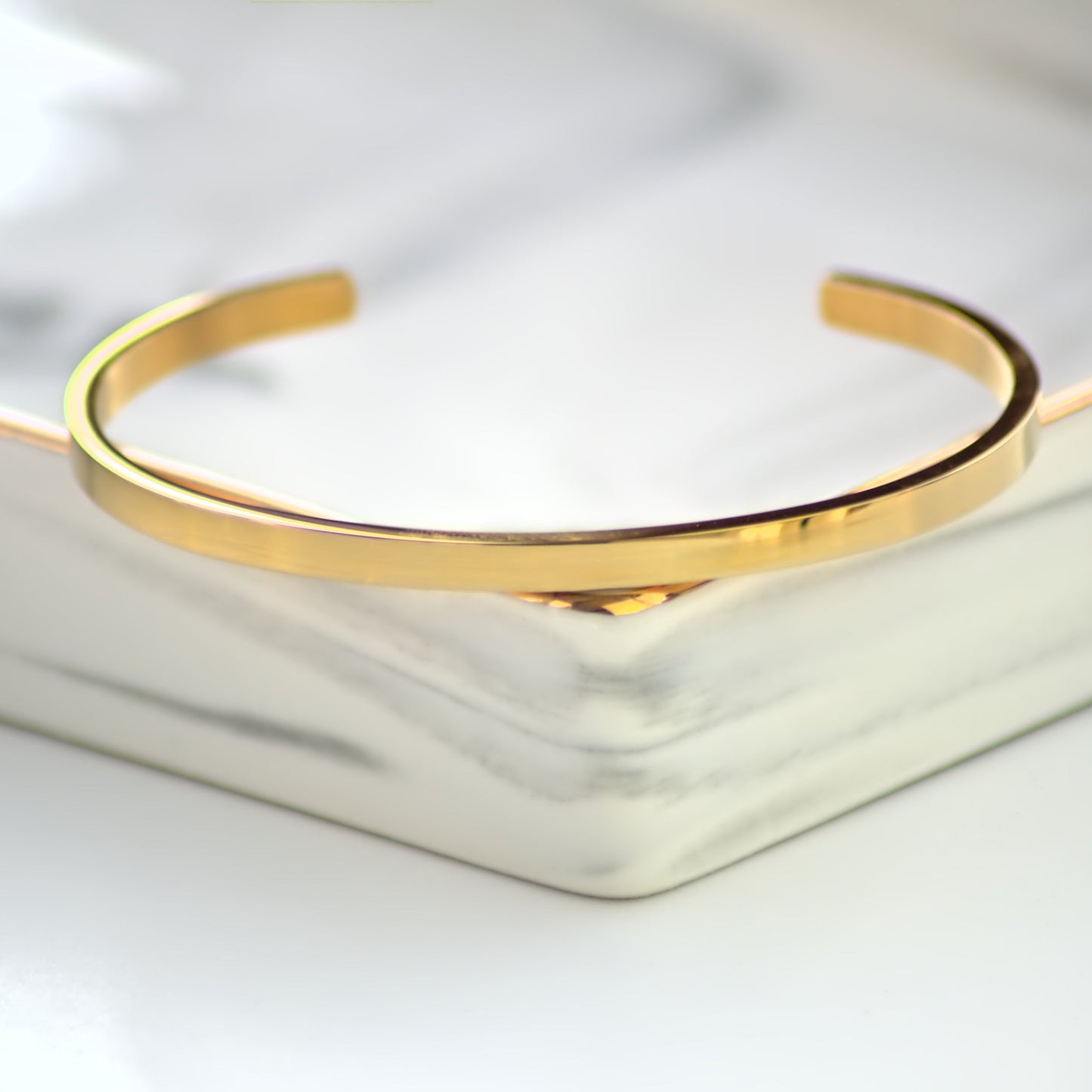 Gold cuff bangle laying on the corner of marble tray. Front profile in focus.