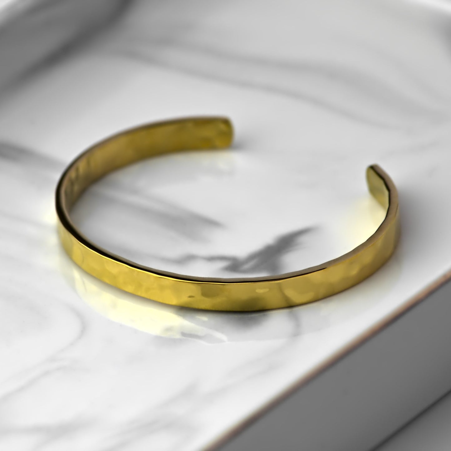 Gold cuff bangle with hammered finish, resting flat on elegant marble tray.