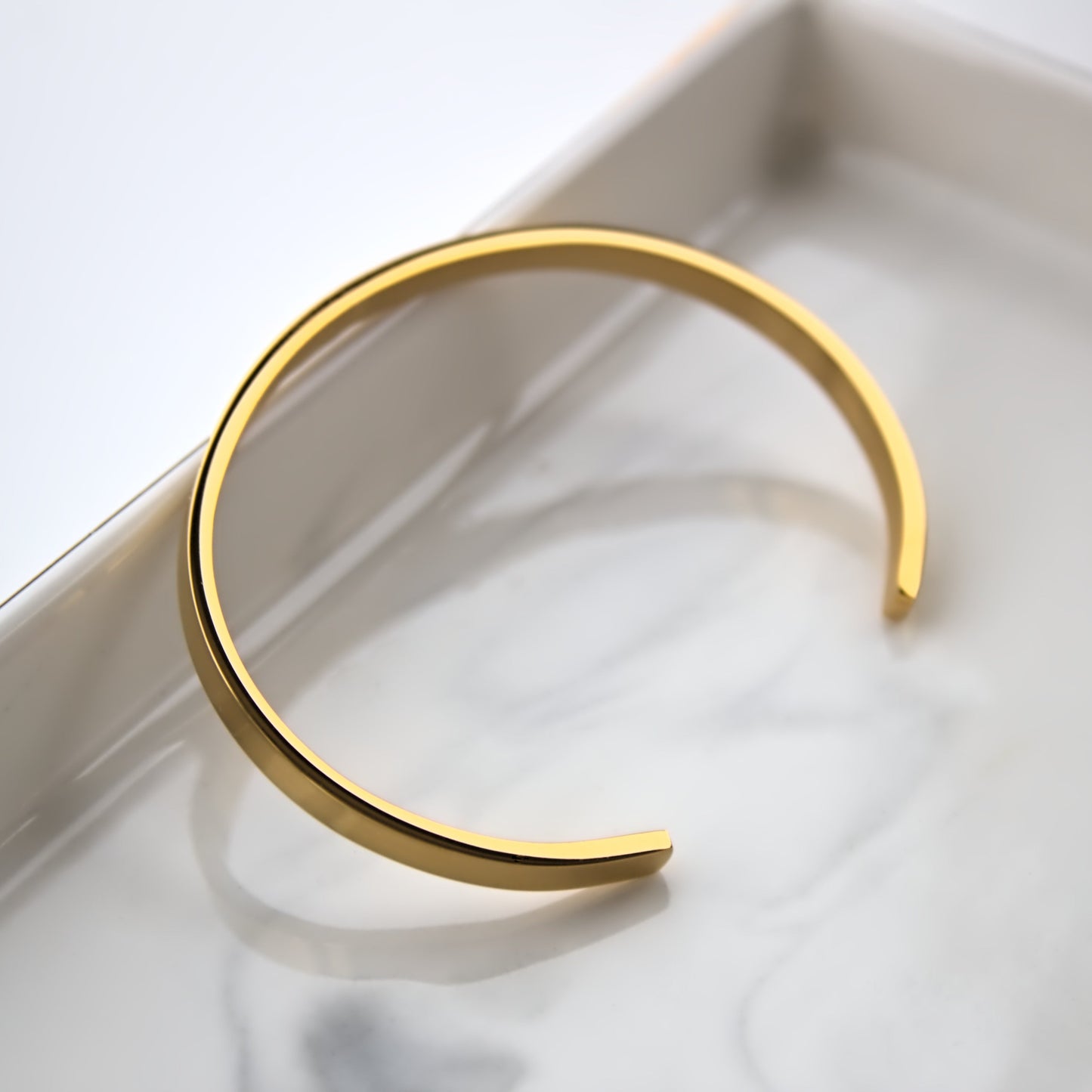 Gold Cuff bangle, leaning on edge of marble tray, showing the full side profile.