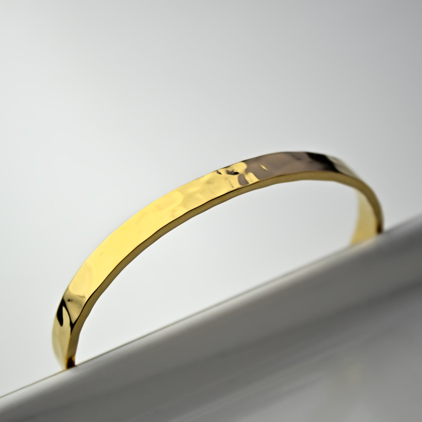 Top side view of gold hammered cuff bangle resting against edge of marble tray