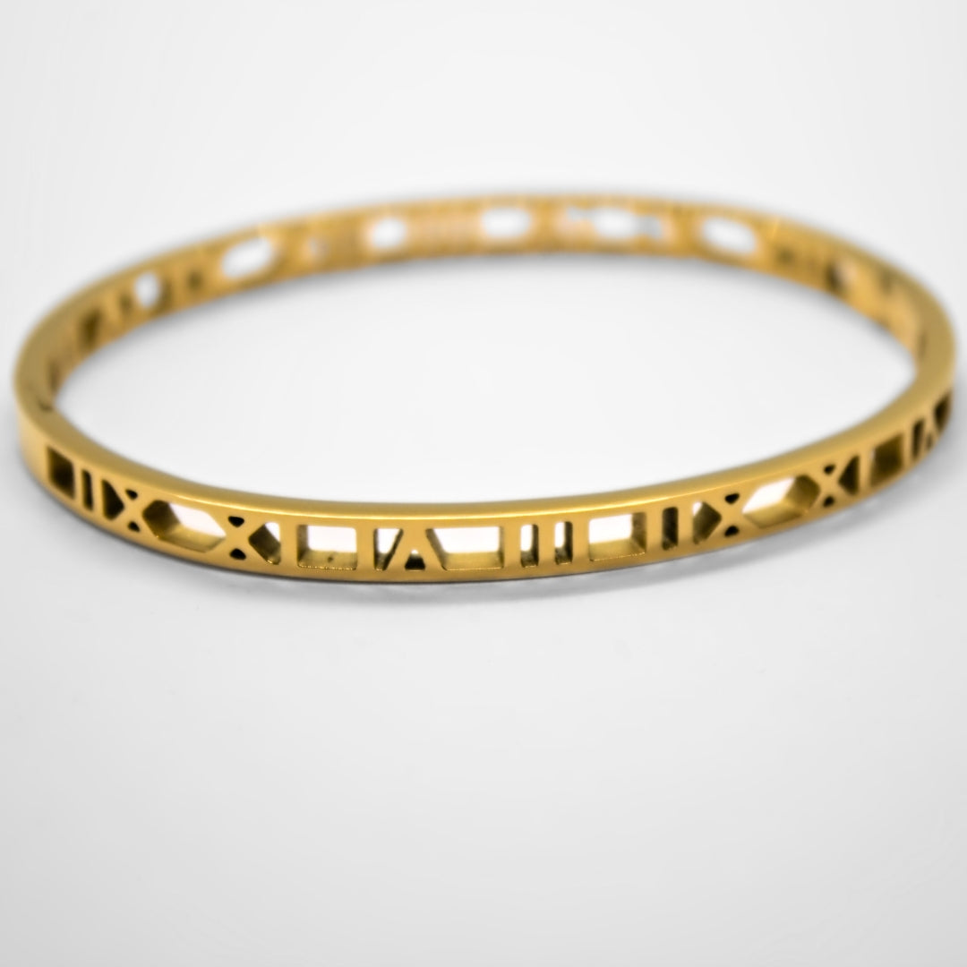 Close up of gold numerals bangle resting on white surface. Showing IIX, XI, IA, III, IIX, XI, IX numbers.