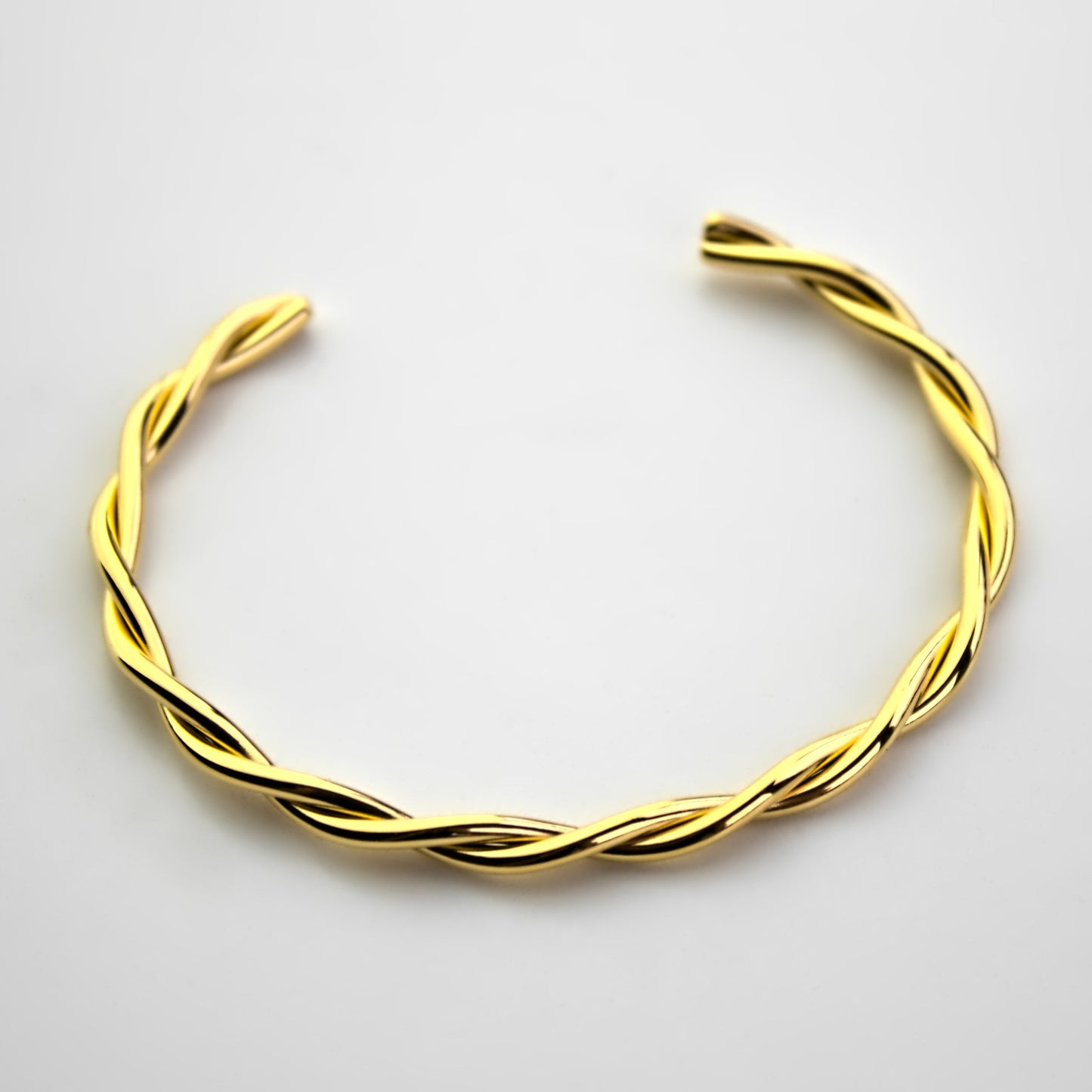 interweaving gold cuff bangle on flat white surface, front view.