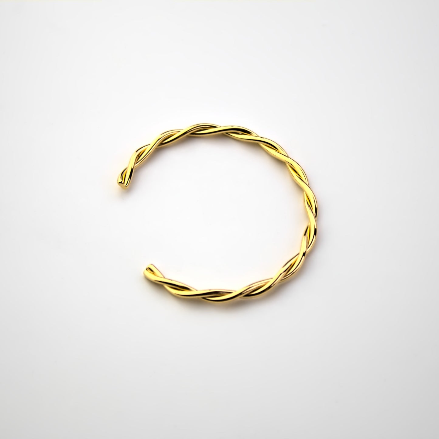 Interweaving gold cuff bangle on white surface, top down view, bangle facing east.