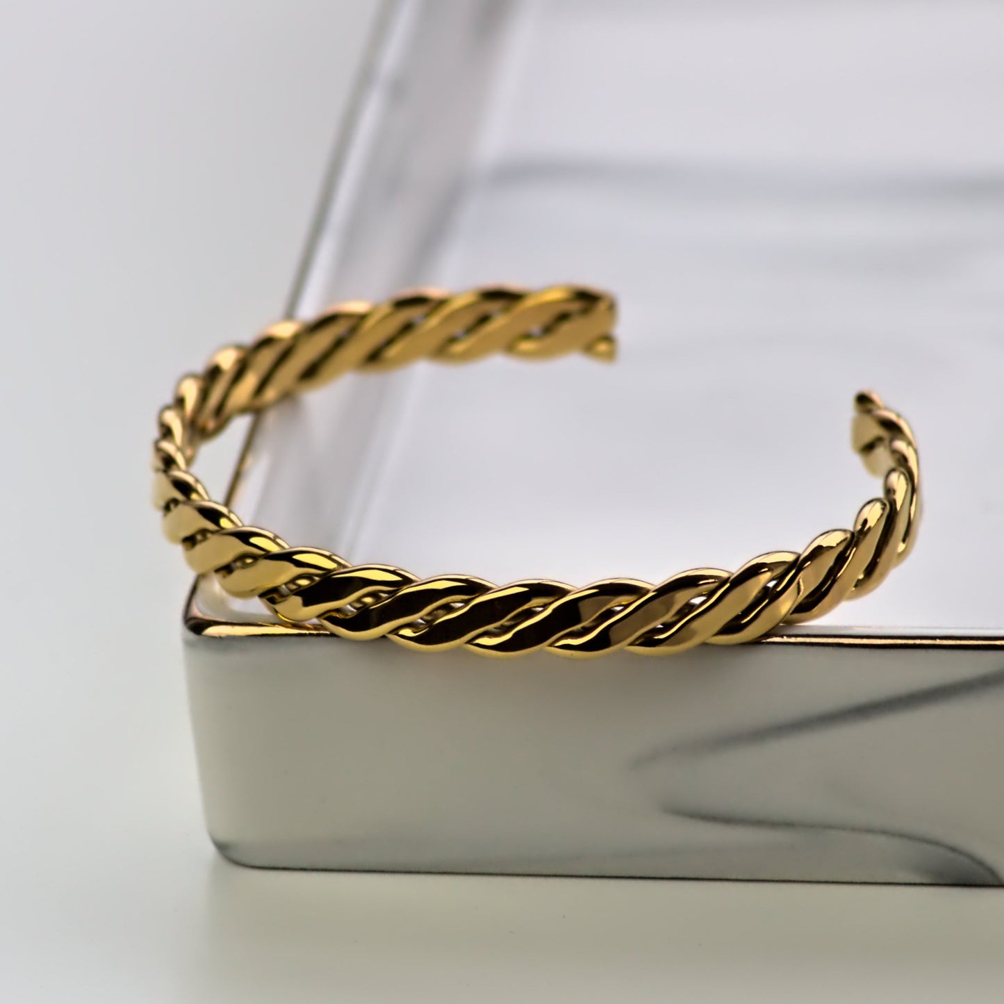 Woven gold cuff bangle front profile, resting on corner of square marble tray.