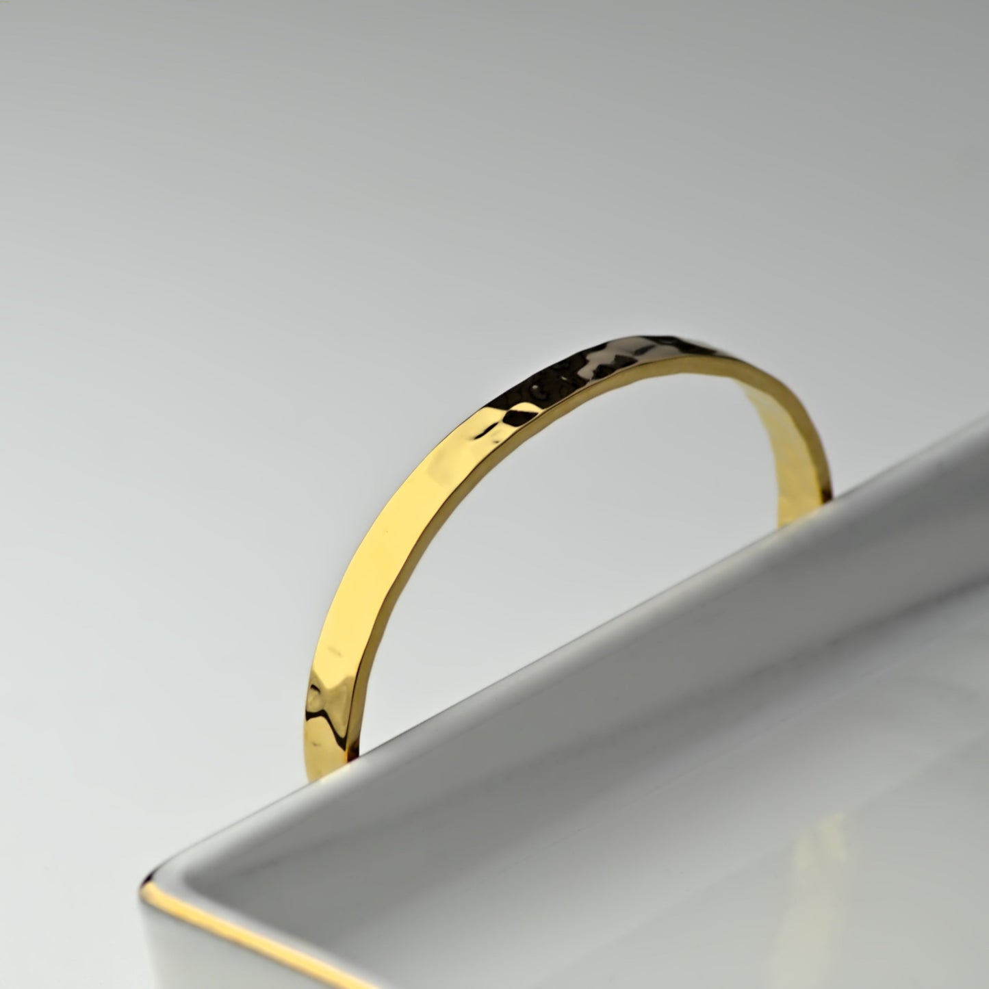 Gold Hammered style bangle sitting behind marble tray, with top half of bangle showing.