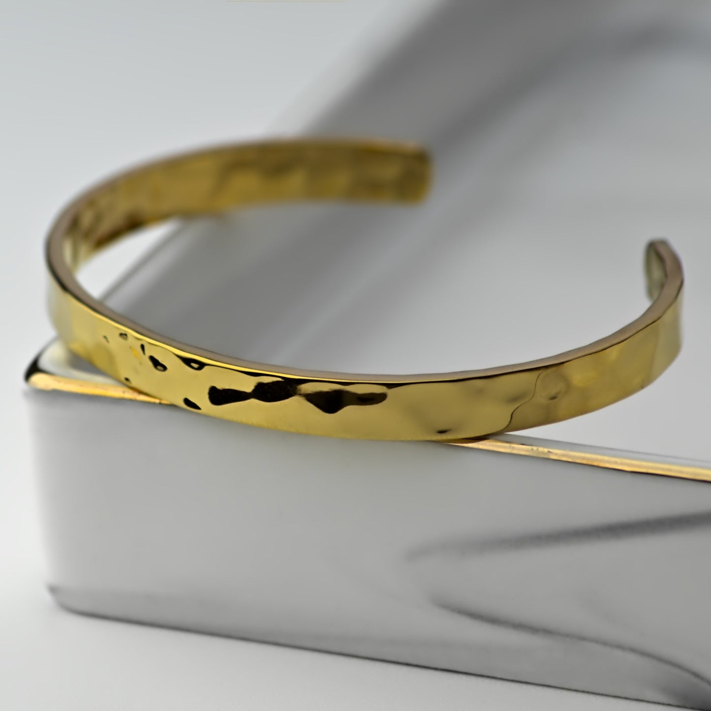 Gold cuff bangle bracelet with hammered style finish, resting on corner of elegant marble tray.