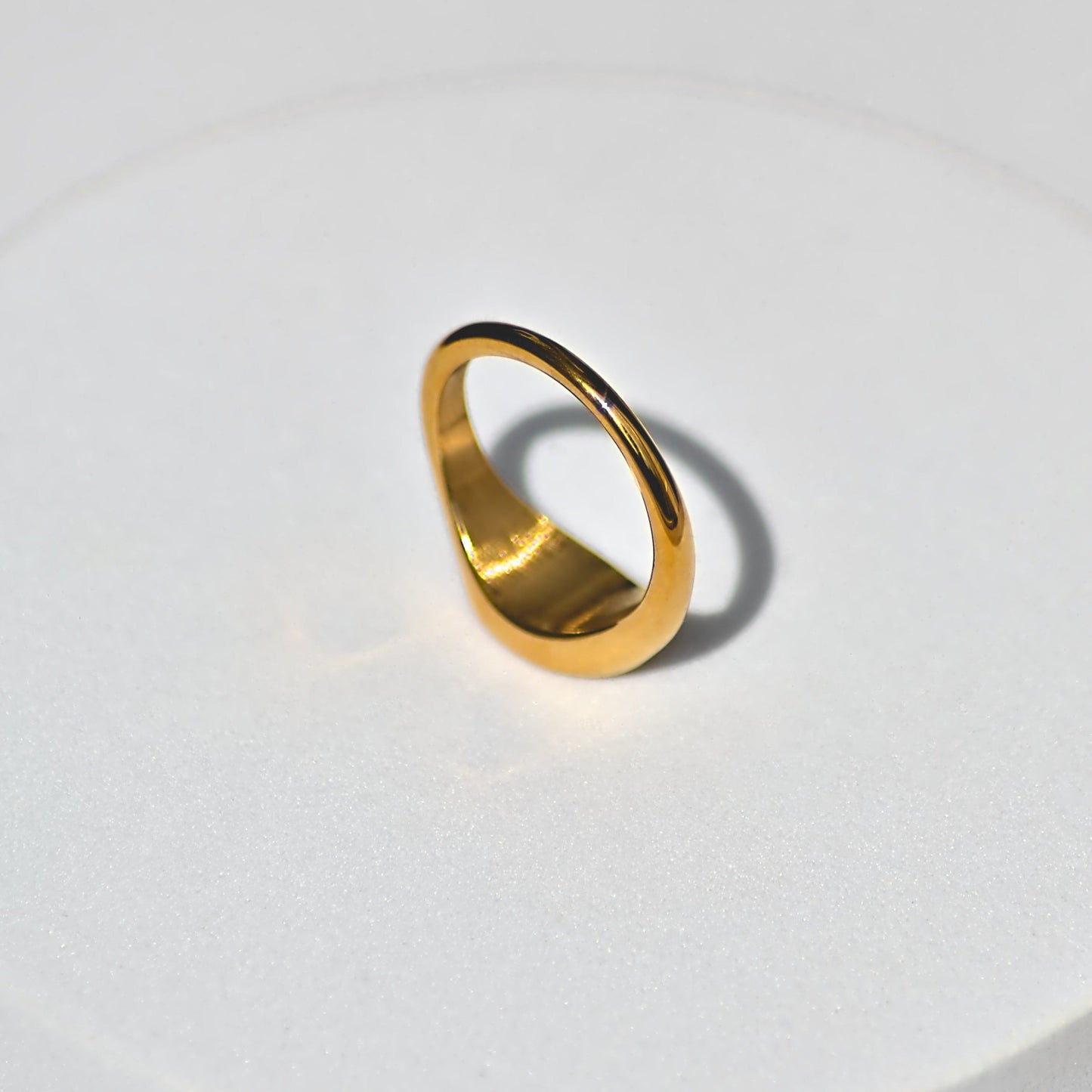 Gold oval signet ring upside down, oval feature flat on white surface. Light shining on ring.