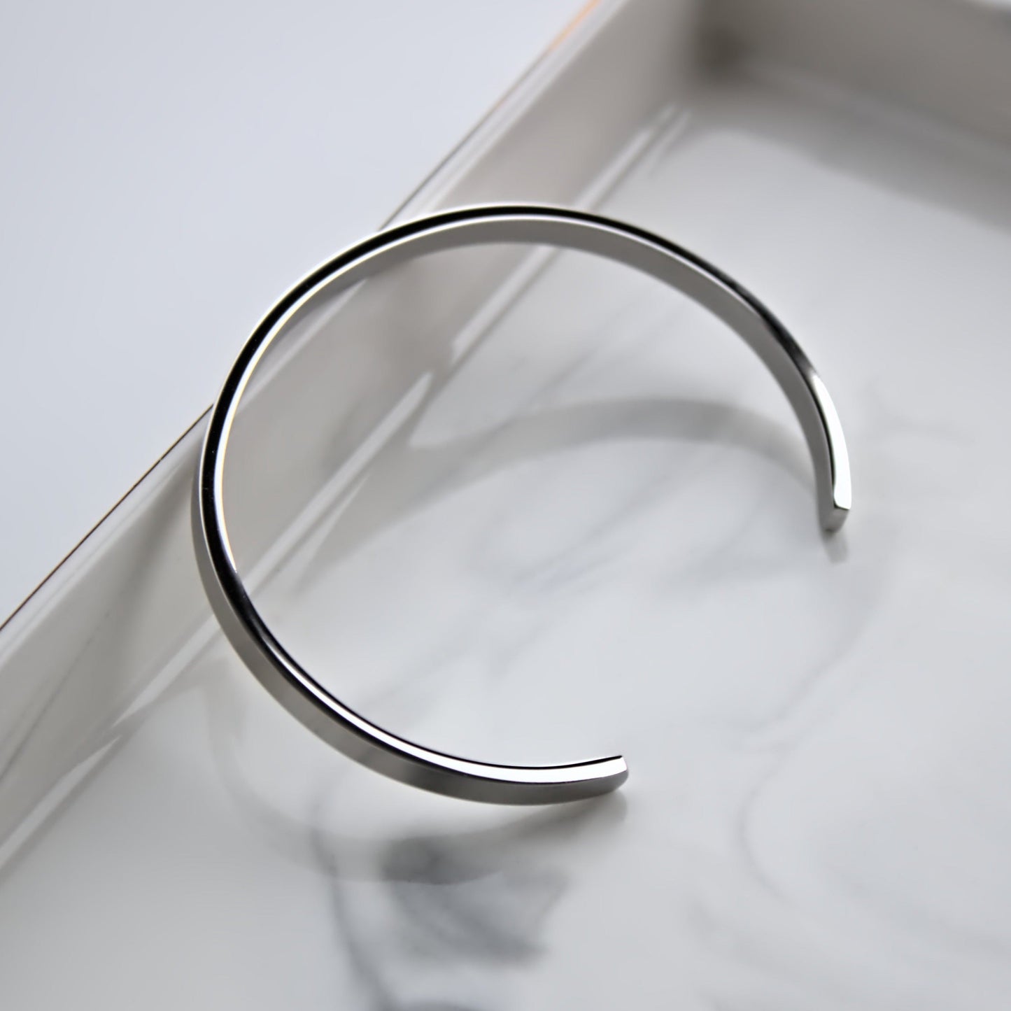 Silver cuff bangle, leaning on edge of marble tray, showing the full side profile.