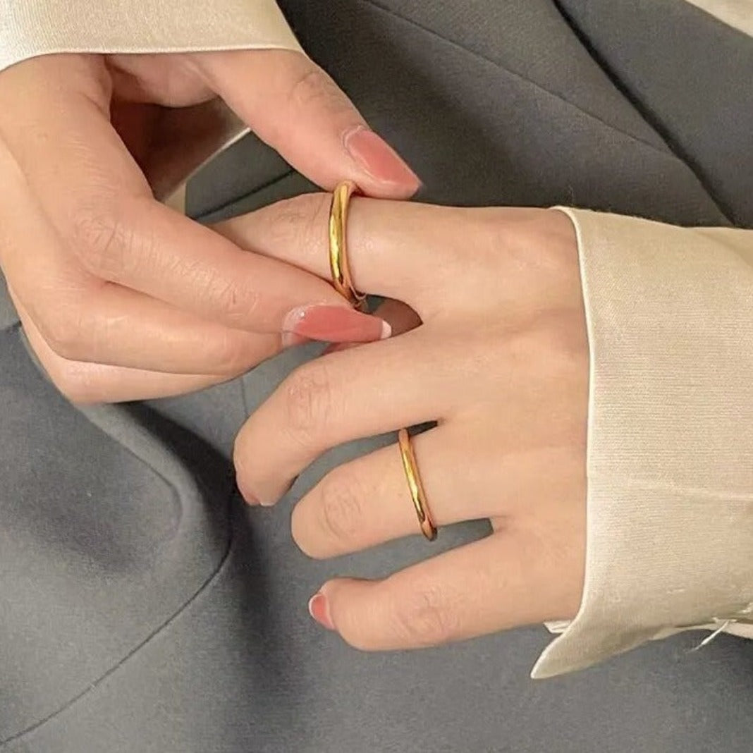 Rings on model, thicker gold ring on index finger, thinner on ring finger. Model slightly holding ring on index finger with other hand.