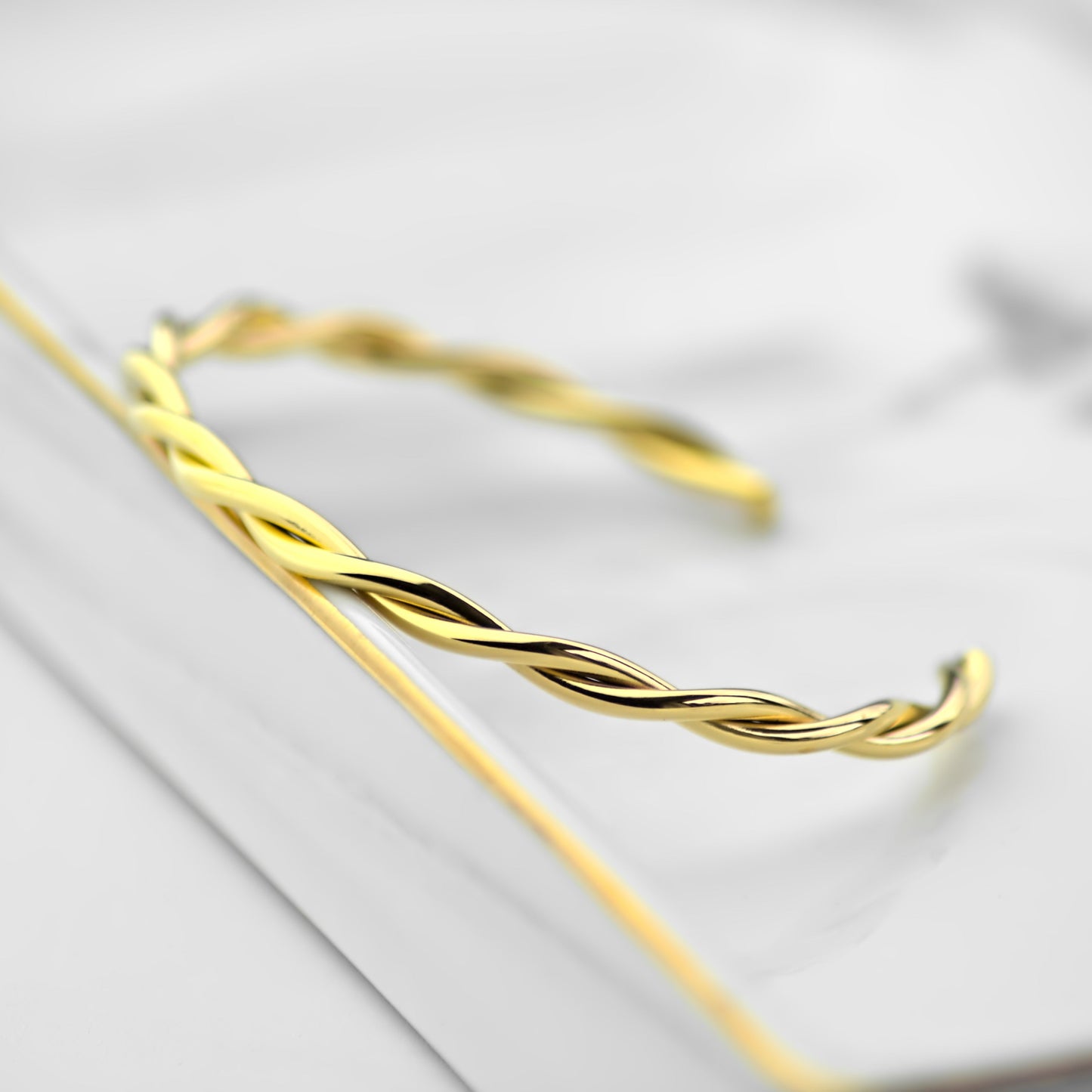 Interweaving gold cuff bangle, resting on side on marble tray. Close up view on front side of bangle.