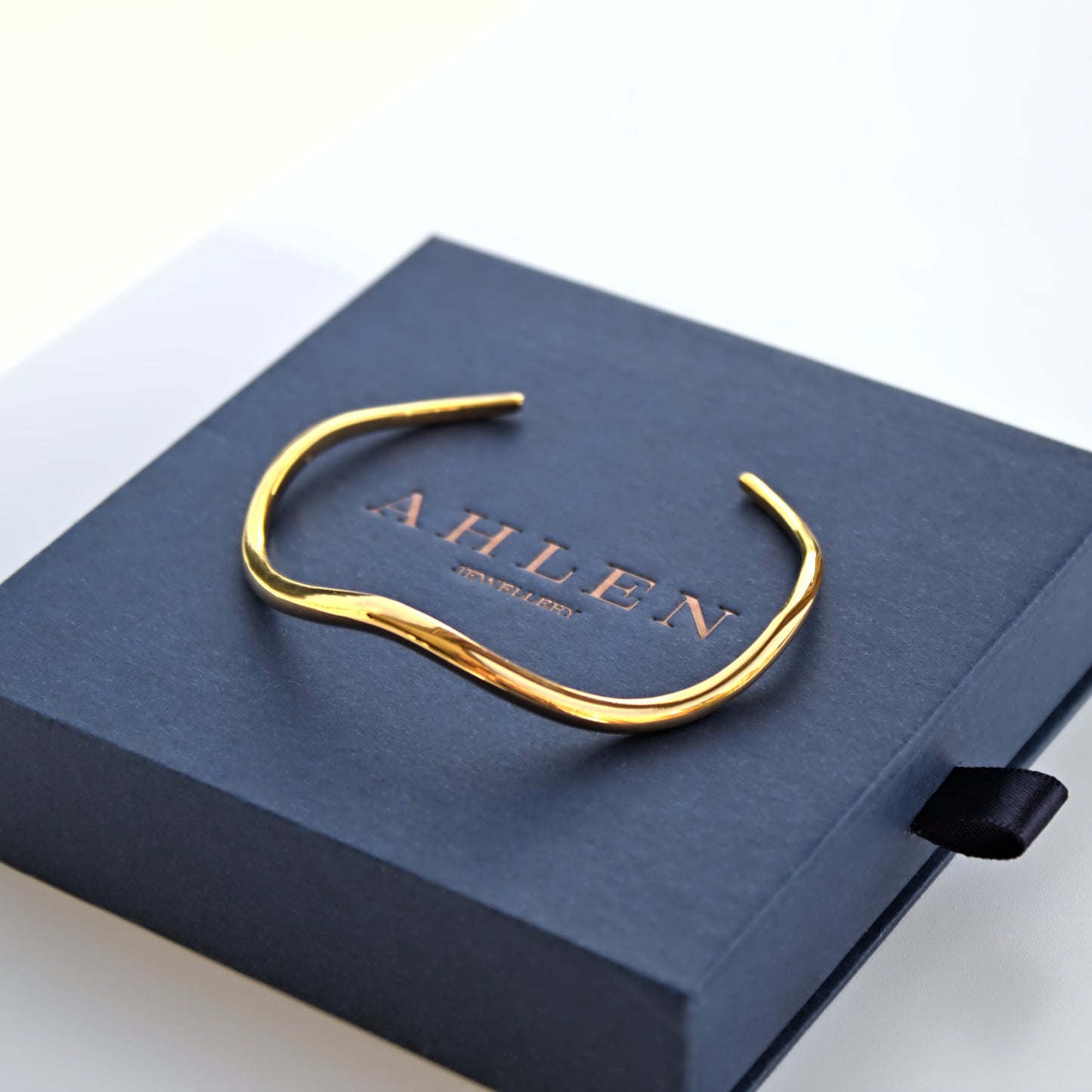 Wave bangle resting on blue Ahlen Jewellery gift box, box sitting on white surface. Frontal view of bangle and box.