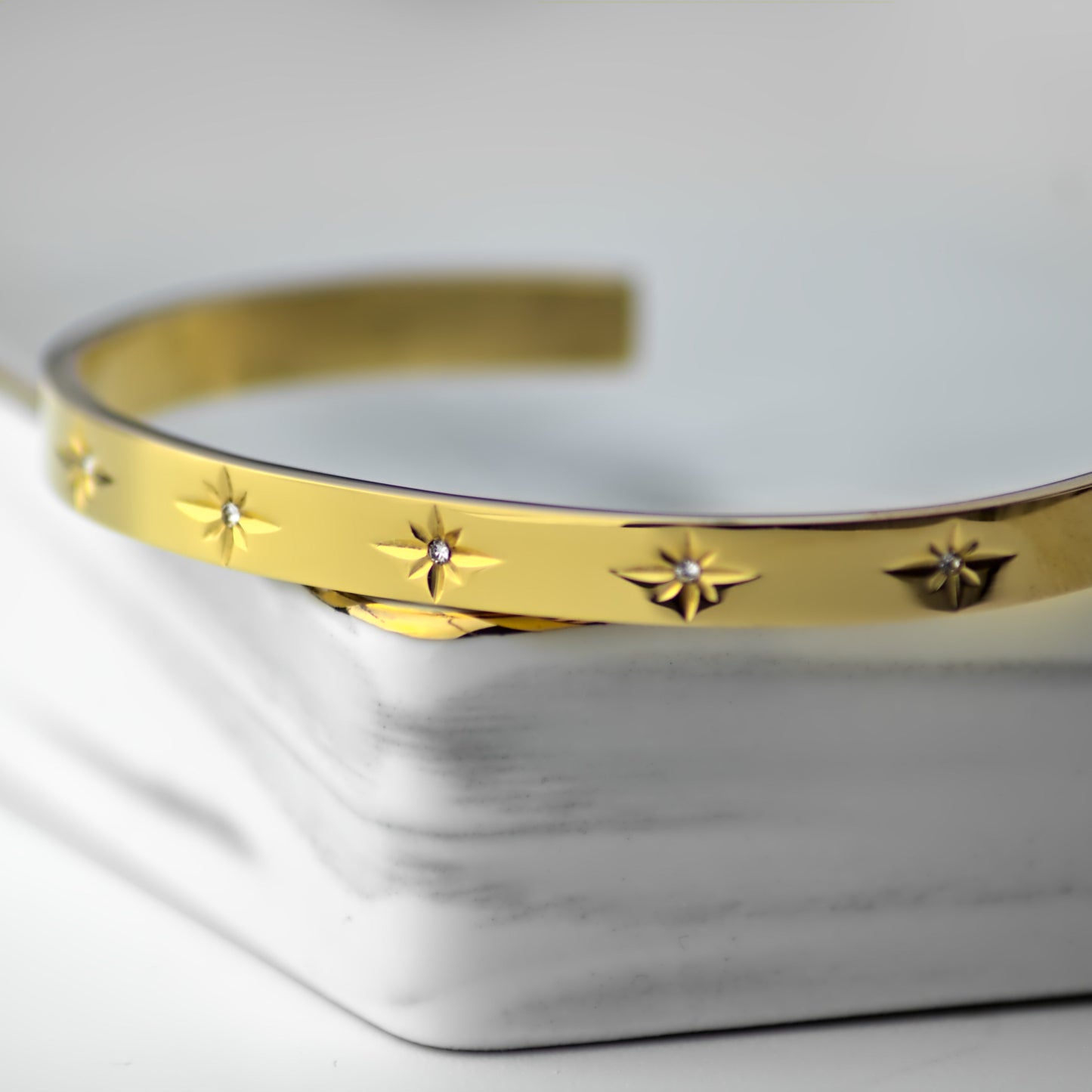 Zircone stone gold bangle resting on corner of elegant marble tray. Close up of stones.