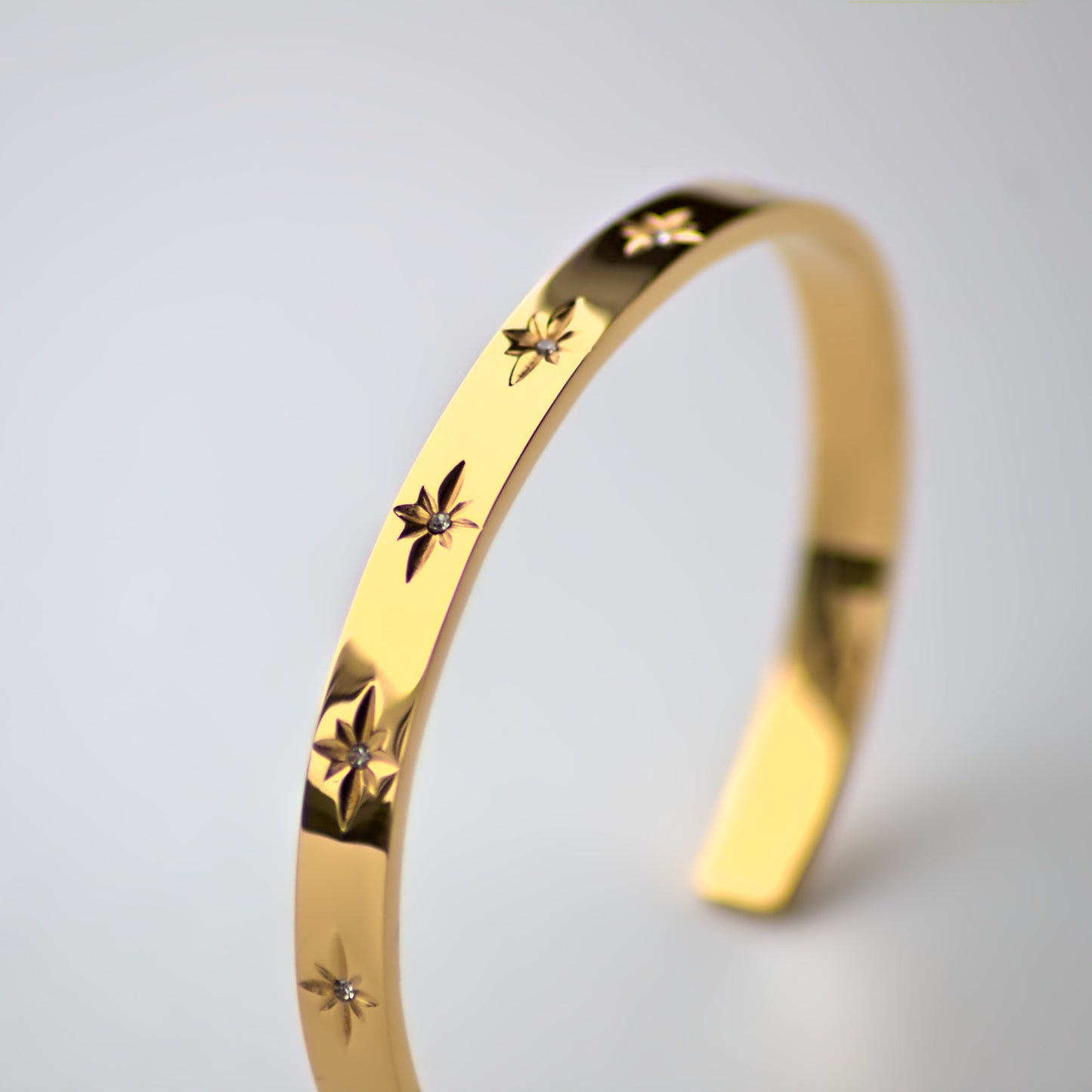 Flat edged cuff bangle featuring zircon stones embedded in star shape pattern, all along the bangle front. Balanced upright, highlighting stones/front of bangle.