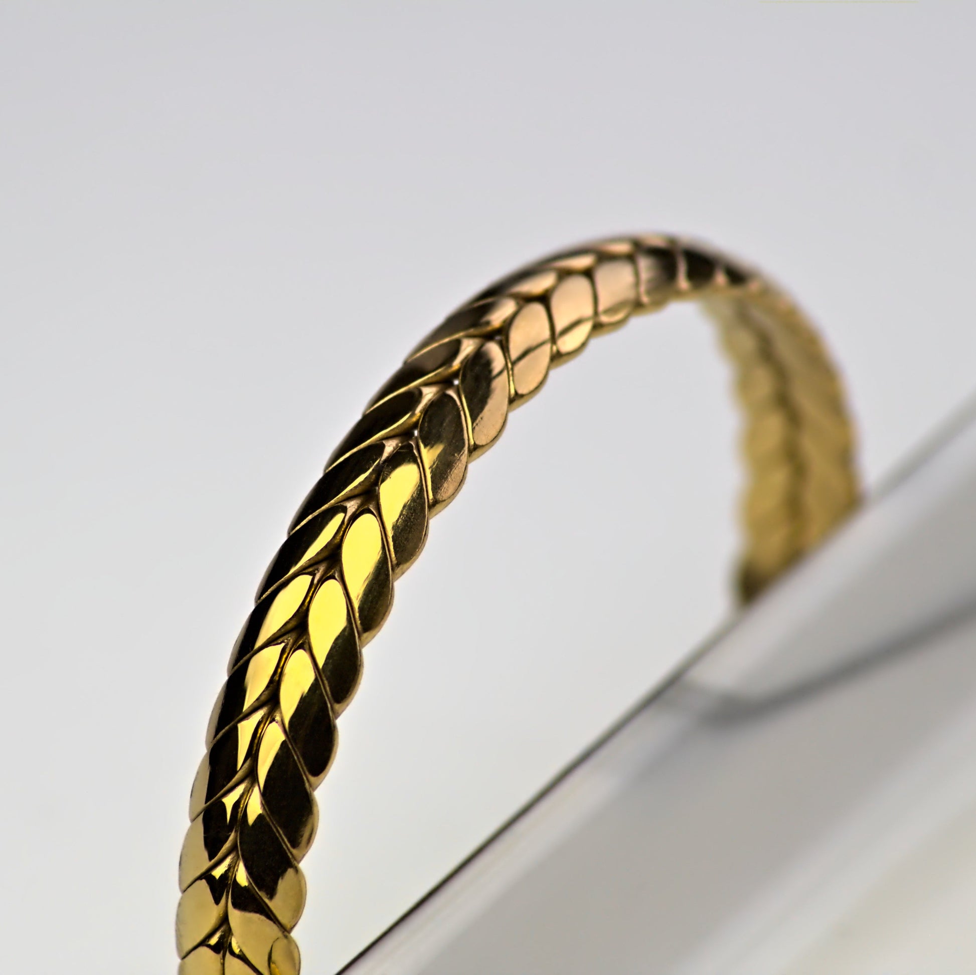 Close up of ear of wheat gold bangle, light reflecting on edge, as it rests against the outside edge of silver colour marble tray.