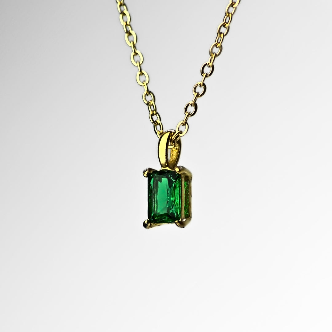 Square emerald green pendant necklace, suspended from top side. Green pendant encased by four corners and hanging from small hoop, with dainty gold chain holding it through the hoop. White background. 