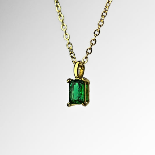 Square emerald green pendant necklace, suspended from top side. Green pendant encased by four corners and hanging from small hoop, with dainty gold chain holding it through the hoop. White background. 