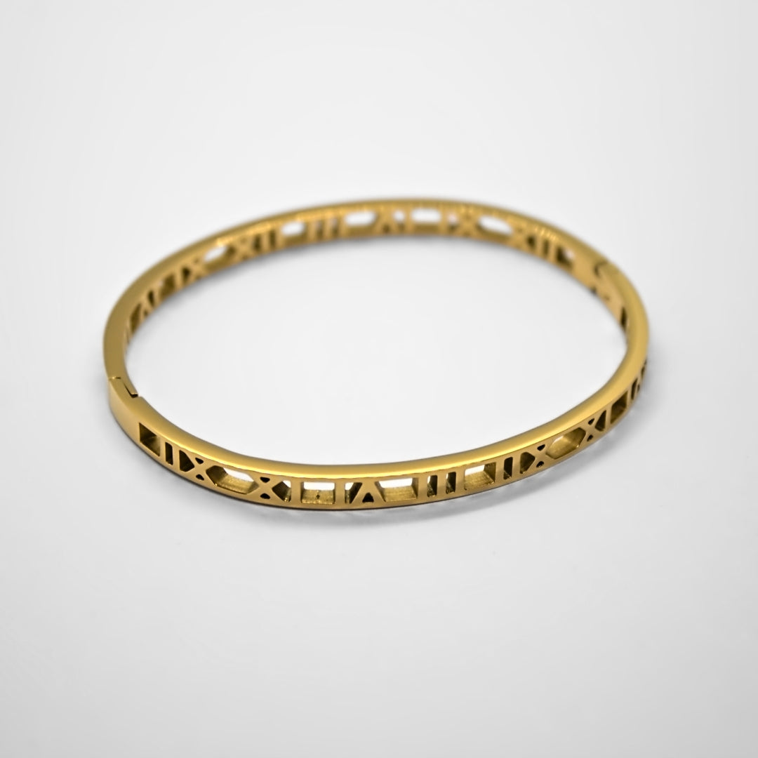 stunning gold closed circle bangle with roman numerals filling the sides. Resting on flat white surface.