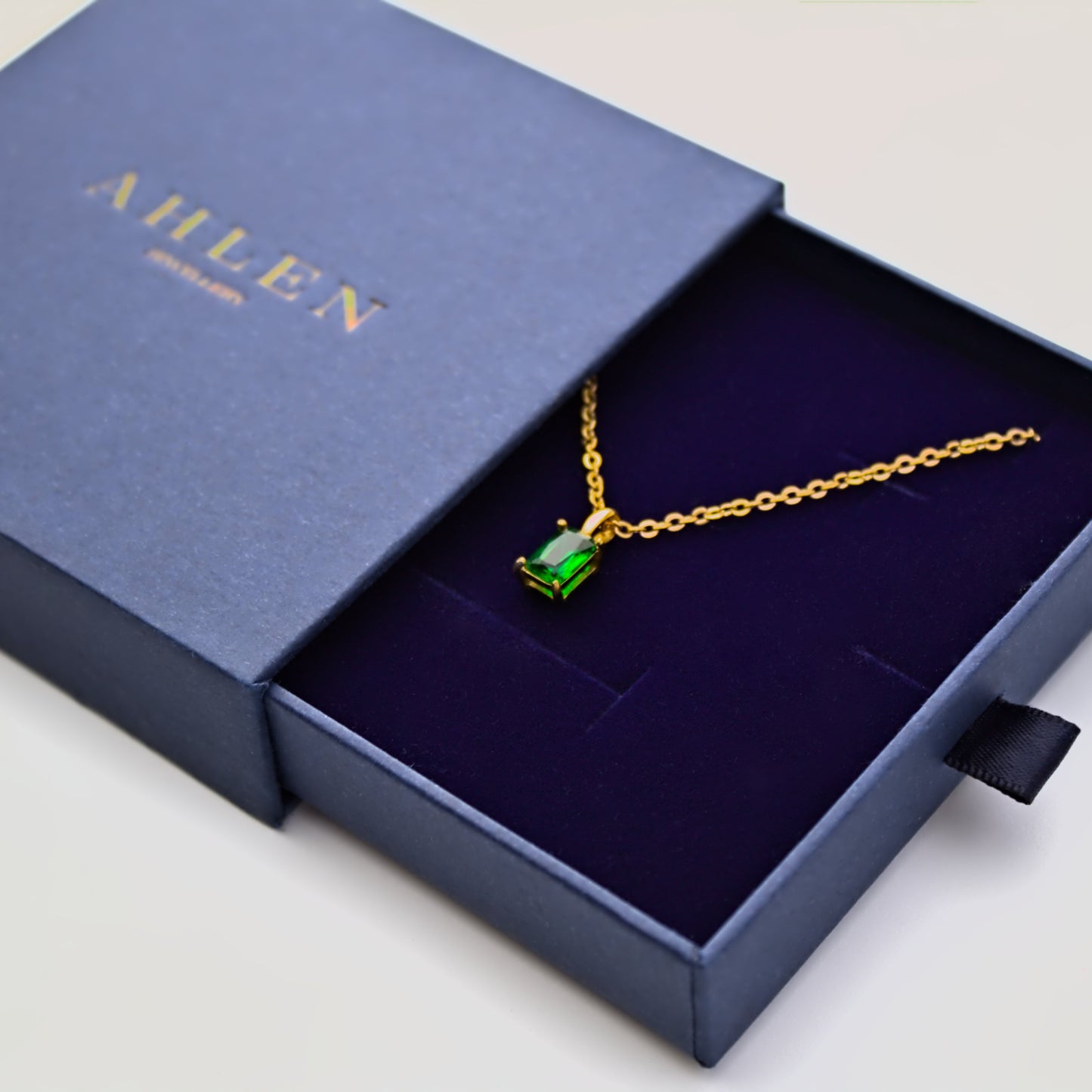 Square emerald green necklace sitting in blue Ahlen Jewellery gift box, professionally presented. Viewing at 45 degree angle. 